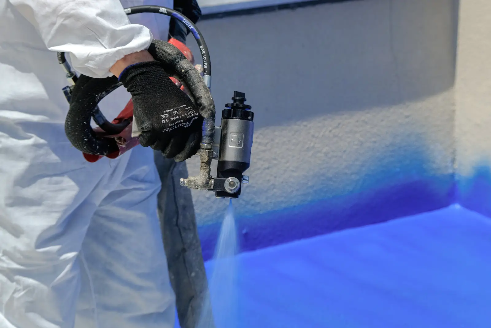 a man in white coveralls painting a wall with blue paint